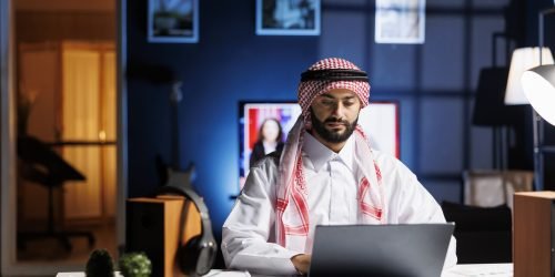 Confident Arab businessman working at a modern desk, typing on his laptop. Muslim guy engaged in browsing, email communication, and wireless connectivity in a calm and professional office setting.